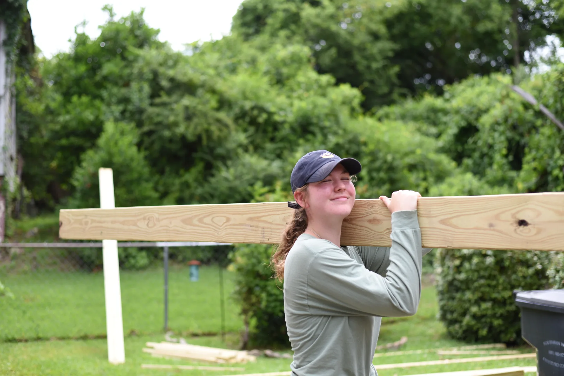 Student carrying lumber with cross in background
